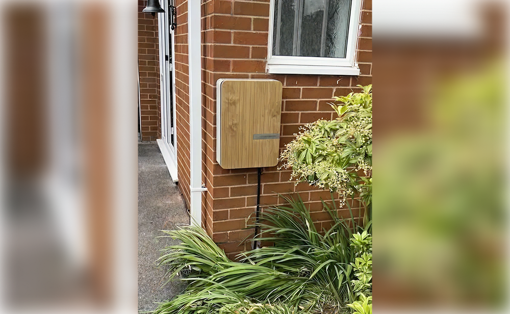 Wooden box mounted on a brick wall near a garden.