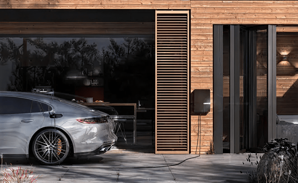 Modern wooden house with a sleek silver car parked outside.