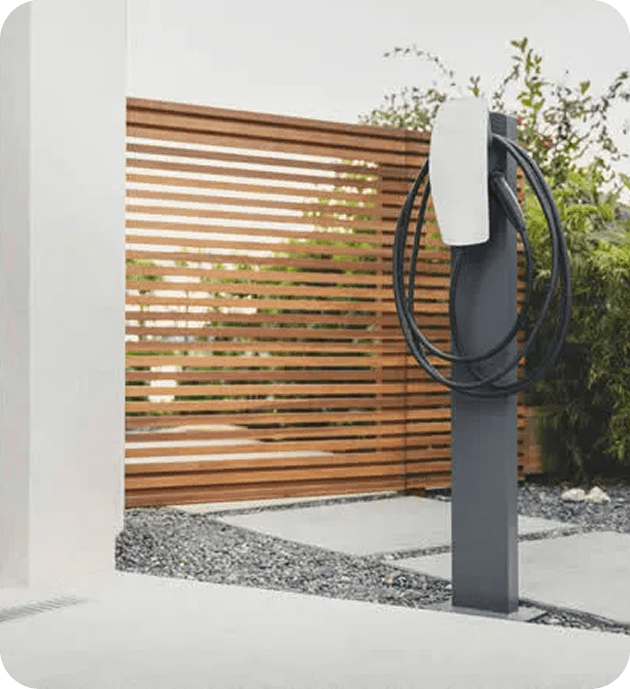 Modern electric vehicle charging station outdoors next to a wooden slatted fence.