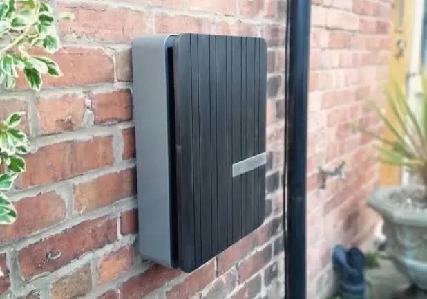 Modern black mailbox mounted on a brick wall outside a house.