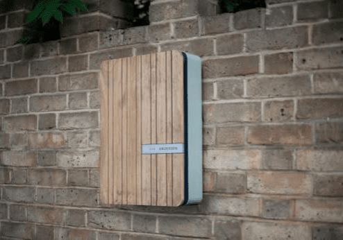 A modern wooden mailbox mounted on a brick wall.